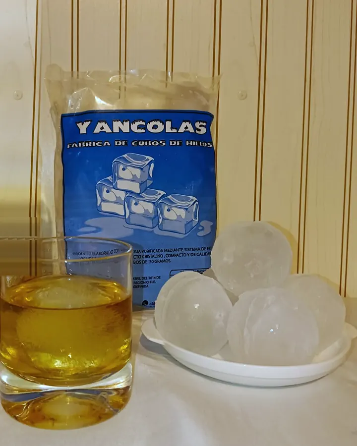 Esfera de hielo en un vaso, junto a una bolsa Yancolas y un plato con más esferas
